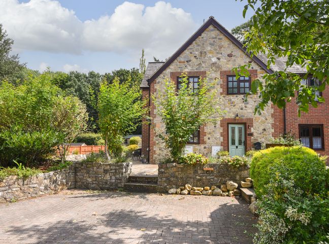 A stone and brick house with a green door surrounded by trees and shrubs at Barley Cottage in Weycroft near Axminster