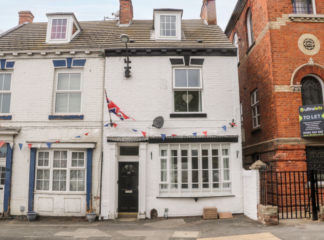 A white two-story brick house with black door number 45 and large windows with bunting and a Union Jack flag at Seashells in Hornsea