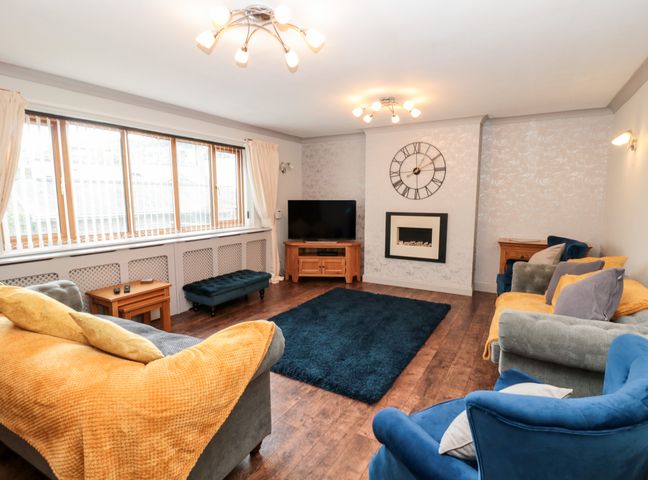 A living room with sofas yellow blankets a blue rug a wall clock a television and wooden furniture at 5 Westwood Road in Scarborough