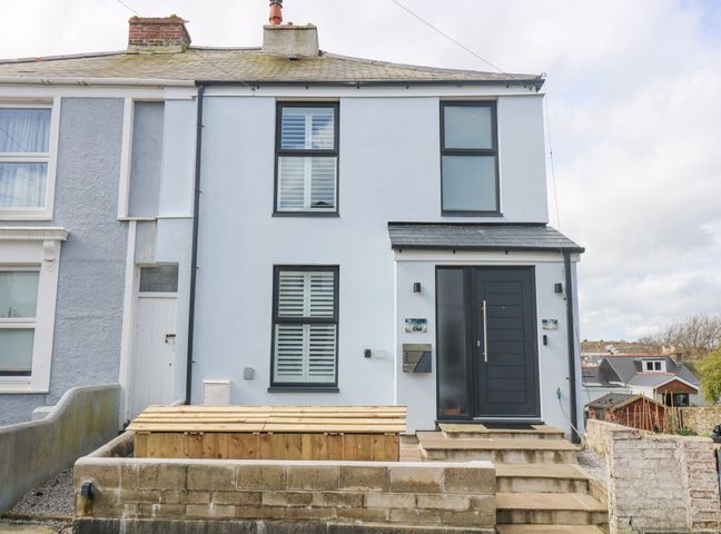 The front exterior of a two-story house with black framed windows a black front door and stone steps at Sailors in Falmouth
