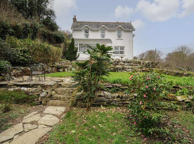 A stone pathway and steps leading to a garden with chairs and a white house in the background at Kirland in St Kew Highway