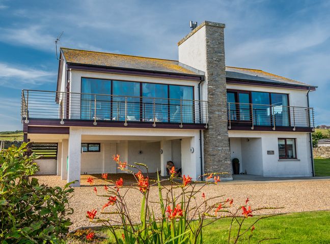 A modern two-story house with a stone chimney and balcony overlooking a gravel driveway and green lawn at The Steading in Longhope