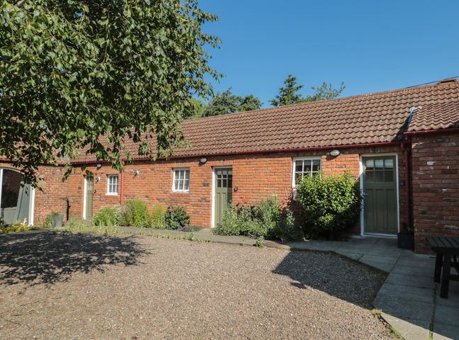 A brick building with three green doors and small windows surrounded by plants and gravel at Cherry Studio in Crookham near Cornhill-On-Tweed