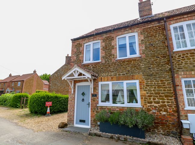 Exterior view of a stone and brick two-story house with a light blue front door and white framed windows at Herbies Cottage in Snettisham