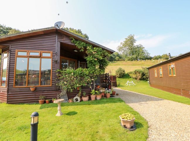 A wooden cabin with potted plants and a gravel pathway on a grassy lawn at 6 Badgers Retreat Tunstall near Richmond