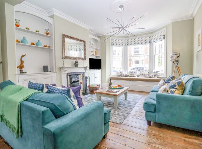 A living room with blue sofas a coffee table and bay window seating at Heron House Southwold