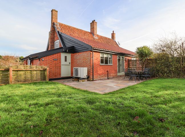 A brick house with red tiled roof a paved patio with a table and chairs and a grassy garden at Pudding Cottage Westleton