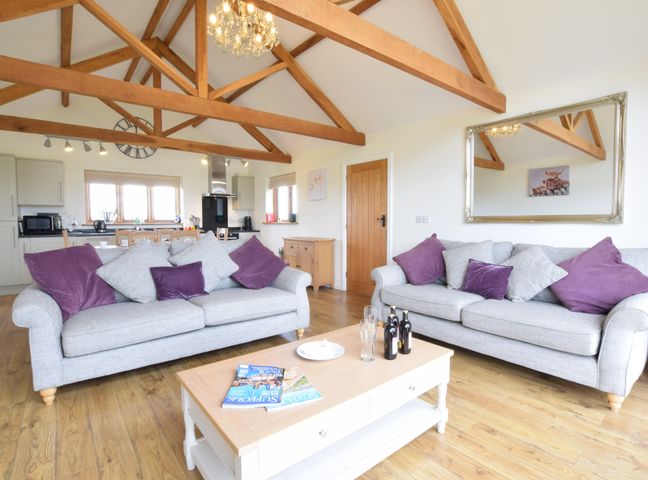 A living room with two grey sofas with purple and grey cushions a wooden coffee table with bottles and magazines and exposed wooden beams at The Mulberry nr Bungay Bungay
