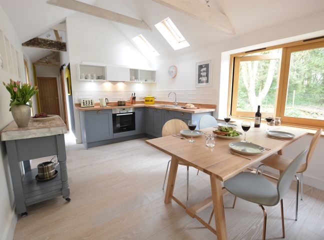 A kitchen with a wooden dining table set for four and gray cabinets under skylights at Red Poll Barn Spexhall Near Halesworth