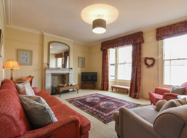 A living room with red sofas a patterned rug a fireplace and large windows at Walton House Southwold