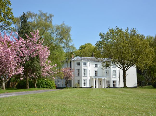 A large white house with columns surrounded by trees and a lawn at Henstead Hall in Henstead near Beccles