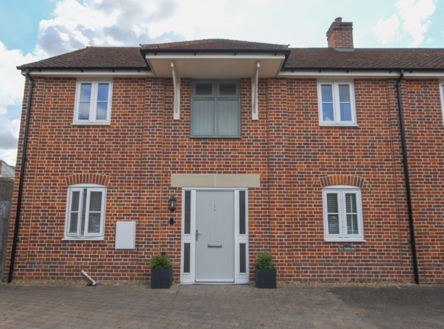 A brick building with white framed windows and a central gray door with two small plants at the entrance at 1 Coconut Cottage Long Melford
