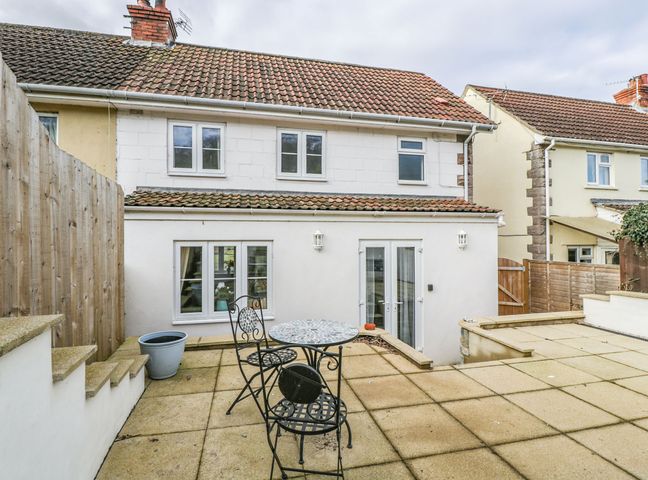 An outdoor patio area with a small round table and two chairs in front of a white two-story house at Celia's View Aller near Langport