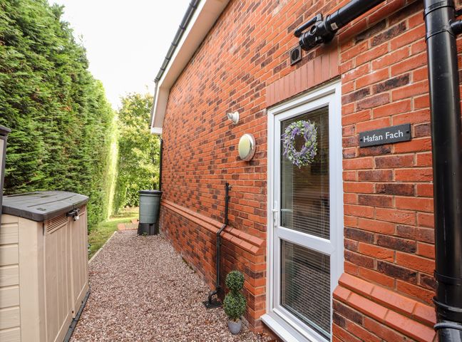 A pathway with gravel alongside a brick building with a door decorated with a wreath and a sign reading Hafan Fach in Mold