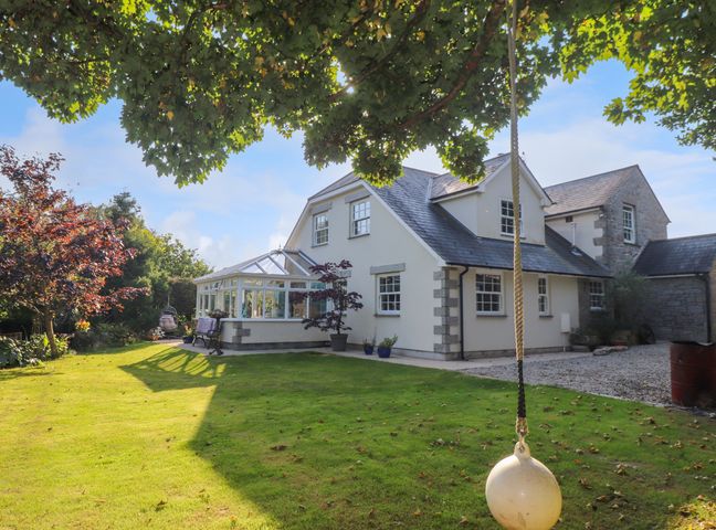 A house with a conservatory and a garden with a swing hanging from a tree at Lower Gadles in Burnthouse near Falmouth