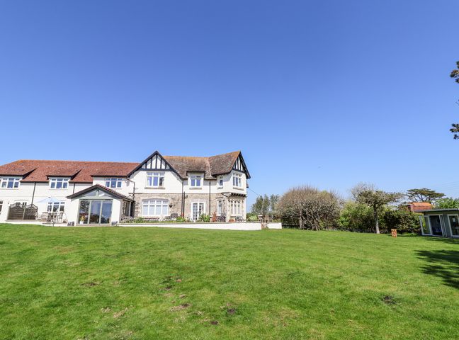 A large white house with a tiled roof and green lawn in front at The Beach House in Beer