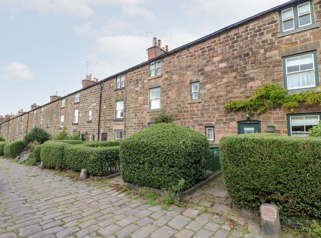 A row of stone houses with green trimmed bushes along a cobblestone street at 16 Long Row in Belper