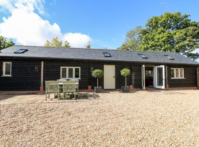 A black wooden house with a gravel yard and outdoor table with six chairs at Barley Cottage in Beauworth near Cheriton