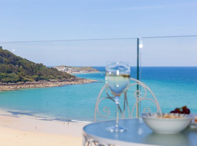 A table with a glass of white wine and a bowl of food overlooking a beach and ocean at Surf and Sand in Carbis Bay