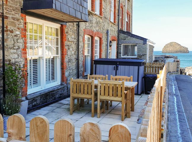 An outdoor patio with a wooden table and chairs next to a stone building by the sea at Salty Sea Dog Trebarwith Strand near Tintagel