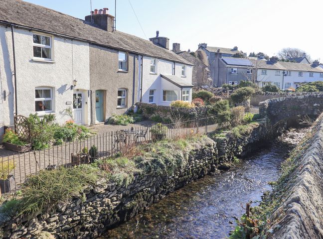 A row of terraced houses along a stone-lined stream with a small stone bridge at Lavender Cottage in Cark In Cartmel