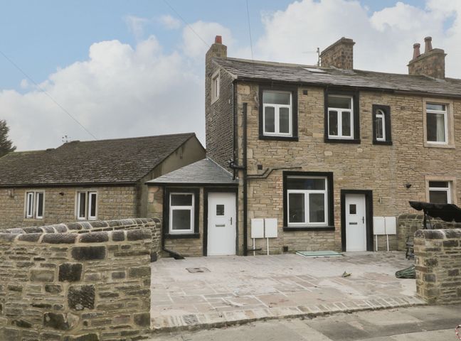 A stone house with white doors and windows and a paved front yard at Moor View in Skipton