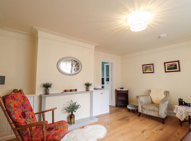 A sitting room with armchairs a mirror on the wall and wooden floor at Tommys in Inverness