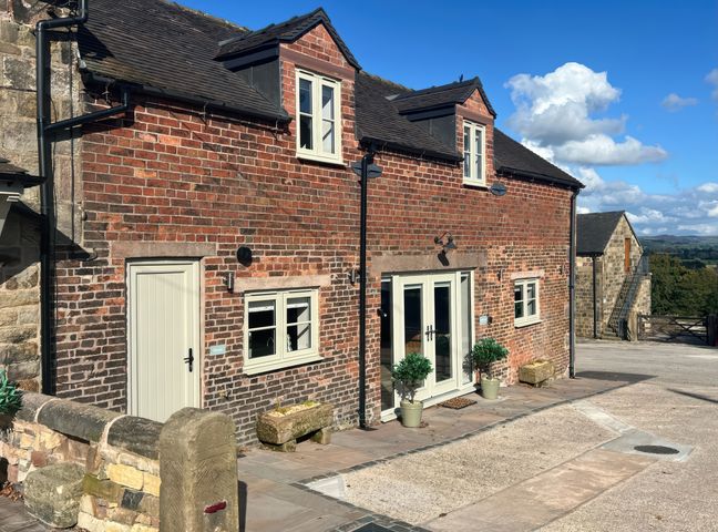 A brick house with white doors and windows and potted plants outside at Small Lane Barn in Blackwood Hill near Endon