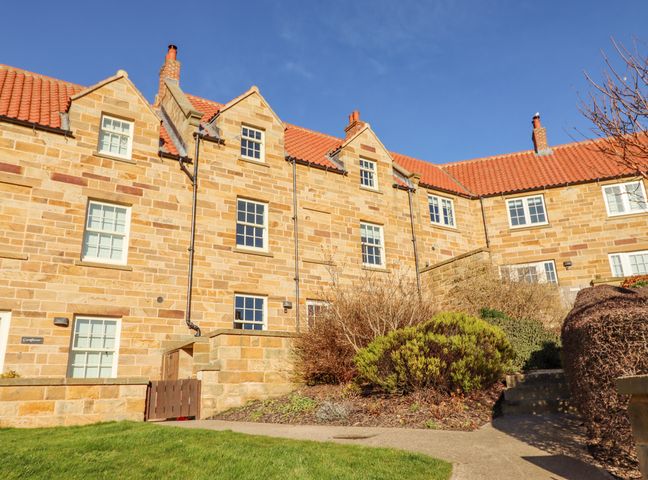 A stone building with multiple windows and a red tiled roof with bushes and a pathway in front at Harebell in Sandsend