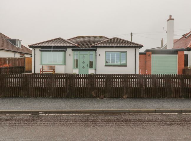 A house with a green door, two windows, a wooden bench, and a wooden fence at Bamburgh Dunes Bamburgh near Seahouses
