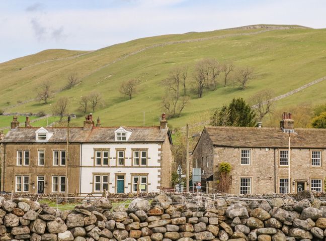 Stone houses with windows and doors in front of a grassy hill and trees at Valley View in Kettlewell