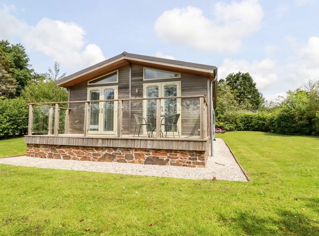 A wooden cabin with glass doors and a small deck with two chairs and a table in a grassy yard at 6 Southern Place in Dobwalls