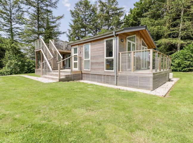 A wooden cabin with an outdoor staircase and glass railings surrounded by grass and trees at 4 Faraway Fields in Dobwalls