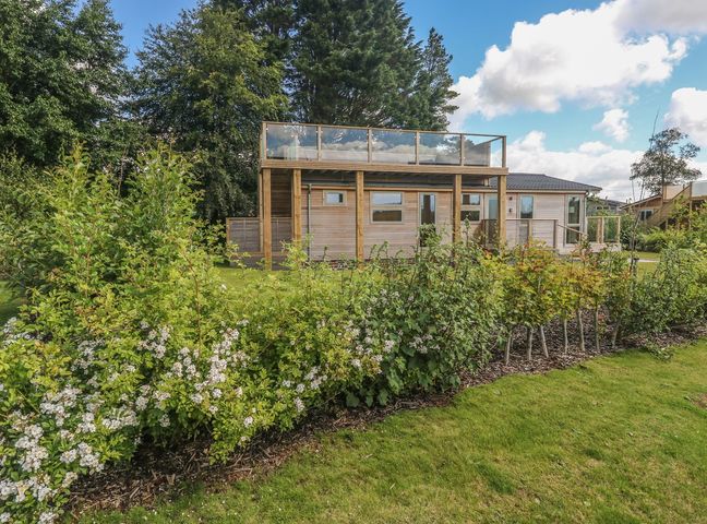 A wooden house with a glass balcony and garden with flowering shrubs at 2 Southern Place in Dobwalls
