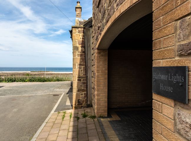 Stone building with an arched entrance and a plaque reading Harbour Lights House by the sea at Harbour Lights House in Seahouses