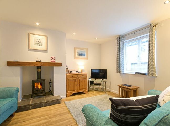 A living room with a wood stove fireplace two blue sofas a wooden cabinet a tv on a stand and a window with curtains at Braidcarr Cottage in Seahouses