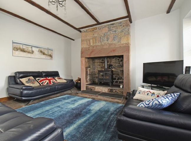 A living room with leather sofas a stone fireplace and a television at Beach Retreat in Seahouses