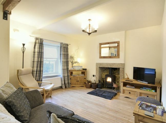 A living room with a wood stove fireplace a TV on a wooden stand and a chair at West End Cottage in Embleton