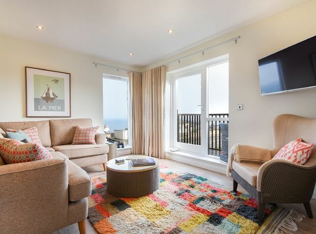 A living room with beige sofas a colorful rug a round coffee table a wall mounted tv and a balcony at Portside in Seahouses
