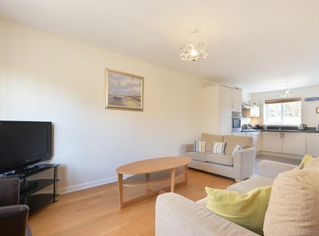 A living room with a beige sofa set a wooden coffee table a television on a stand and a kitchen area at Coast View in Beadnell
