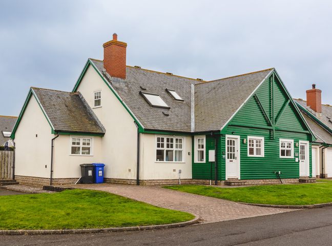 A house with white and green exterior walls two chimneys and a driveway at Armstrong Cottages No30 Bamburgh