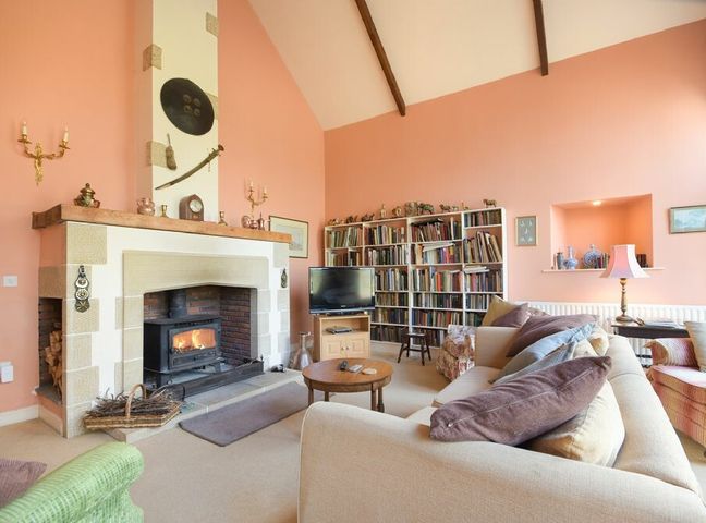 A living room with a fireplace a television bookshelves and sofas at Craster Tower Coach House in Craster