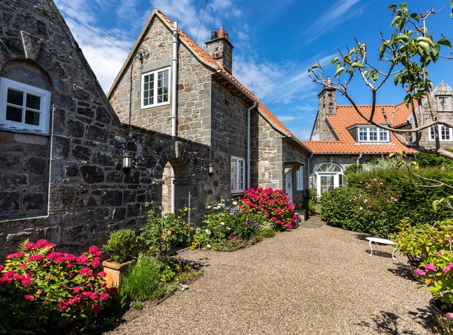 A stone house with red roof tiles a stone wall and flowers in a garden at Mid Cote Shoreston near Bamburgh