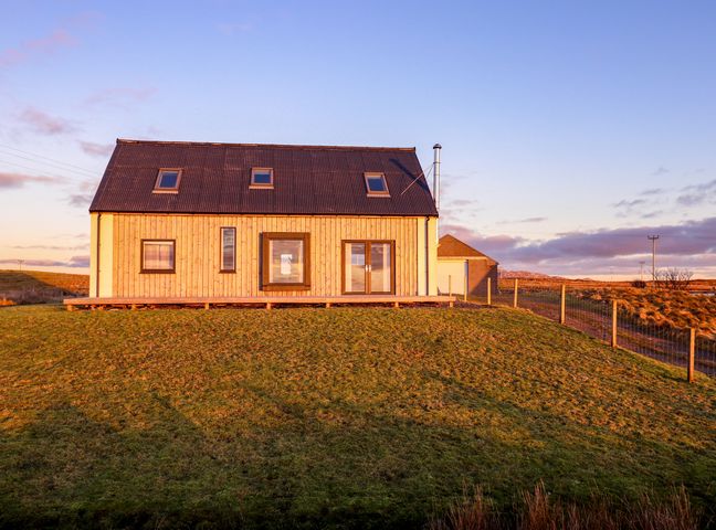 A wooden house with a pitched roof and skylights on a grassy hill at Heatherlea Carinish near Lochmaddy North Uist