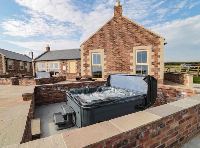 An outdoor hot tub with steps surrounded by brick walls and a brick house in the background at Smithy Cottage in Embleton