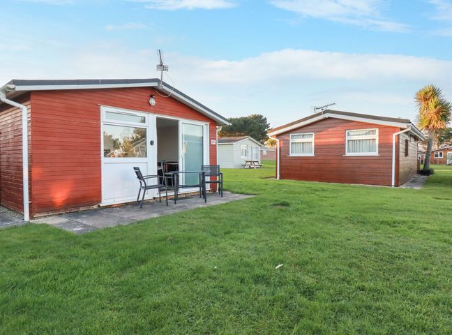 Two red wooden bungalows with white framed windows and doors on a grassy lawn at 171 Atlantic Bays in St Merryn