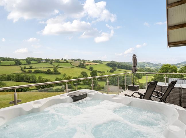 An outdoor area with a hot tub and chairs overlooking the countryside at Bwncath in Garthmyl