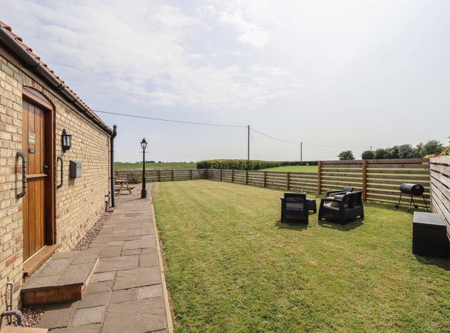 A fenced garden with lawn chairs grill and picnic table outside a brick building at Tawny Cottage in Alford