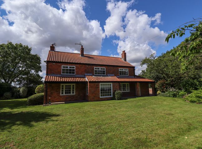 A brick house with a tiled roof surrounded by a garden with grass and trees at Moon Field Lodge in Epworth