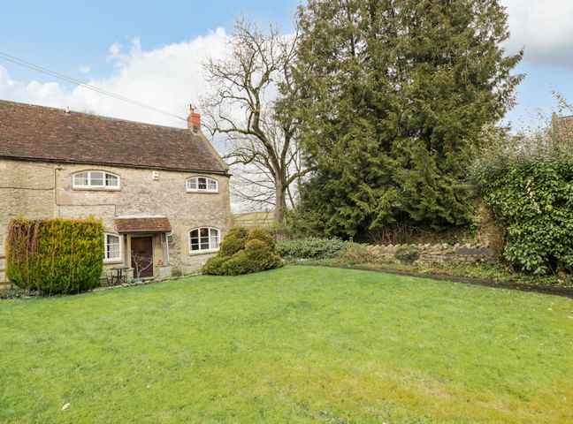 A stone cottage with a tiled roof surrounded by lawn and trees at Field Cottage in Shepton Mallet